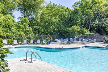 A pool surrounded by trees and chairs.